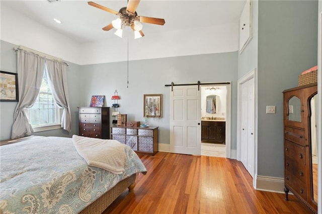 bedroom featuring a barn door, connected bathroom, baseboards, and wood finished floors