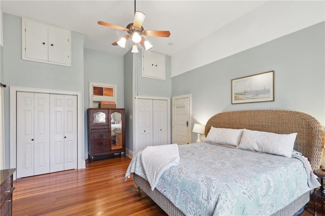 bedroom with ceiling fan, high vaulted ceiling, wood finished floors, and two closets