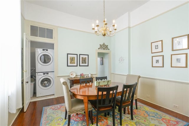 dining space featuring a wainscoted wall, dark wood-style flooring, stacked washer / dryer, and an inviting chandelier