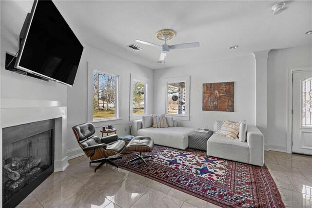 living room featuring ceiling fan, a fireplace, visible vents, baseboards, and ornate columns