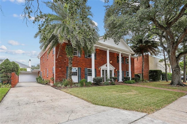 neoclassical home with a garage, a front yard, an outbuilding, and brick siding