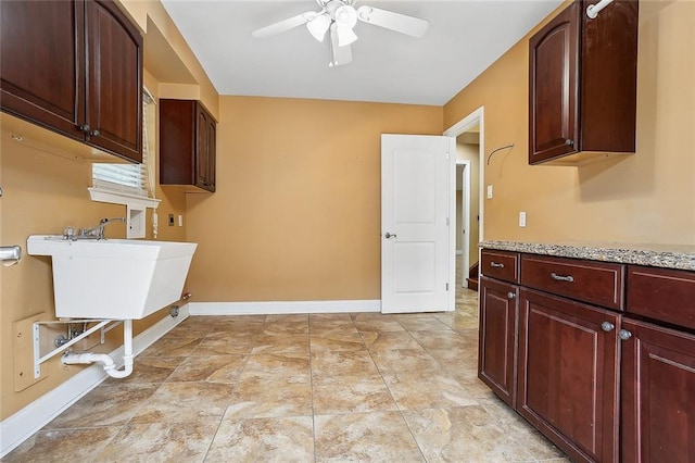 laundry area featuring a ceiling fan, cabinet space, baseboards, and a sink