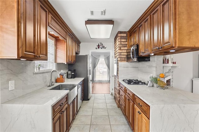 kitchen with appliances with stainless steel finishes, brown cabinetry, a sink, and visible vents