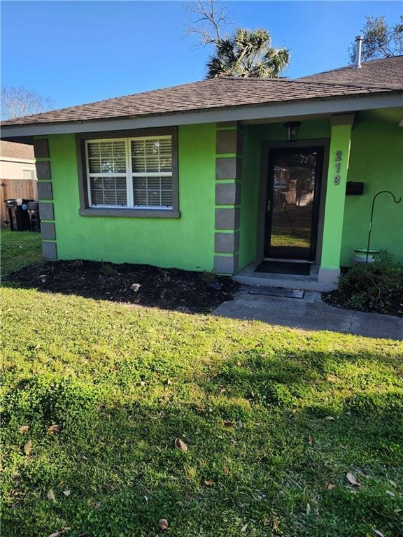 view of exterior entry with a yard, roof with shingles, and stucco siding