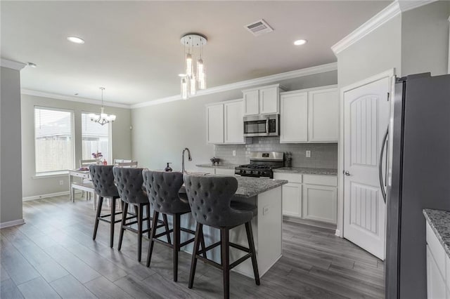 kitchen featuring stainless steel appliances, light stone countertops, white cabinetry, and decorative light fixtures