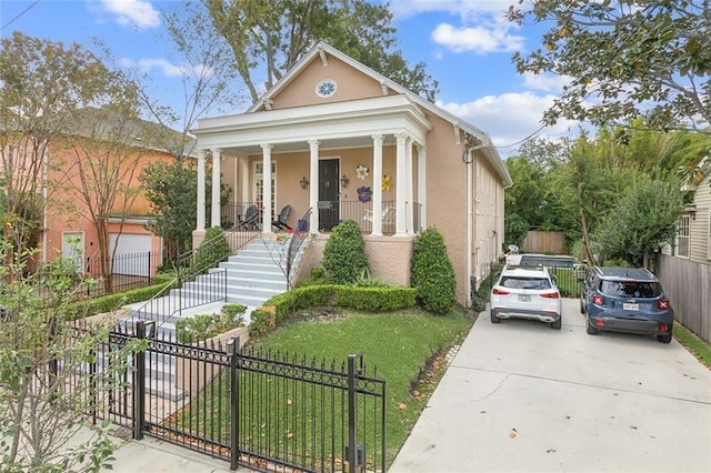 greek revival house featuring a fenced front yard, stucco siding, a porch, a front lawn, and stairs