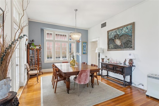 dining space featuring light wood-type flooring, baseboards, visible vents, and a notable chandelier