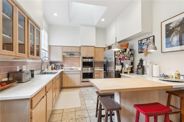 kitchen featuring stainless steel appliances, light brown cabinets, a sink, a peninsula, and a kitchen breakfast bar