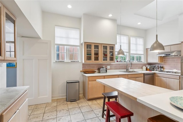 kitchen with under cabinet range hood, a breakfast bar, a sink, and tasteful backsplash