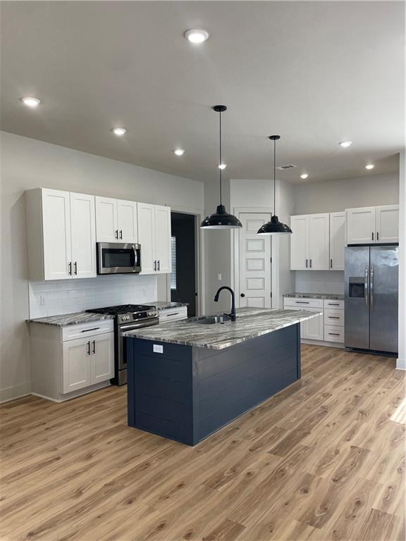 kitchen featuring stainless steel appliances, white cabinets, decorative light fixtures, and an island with sink