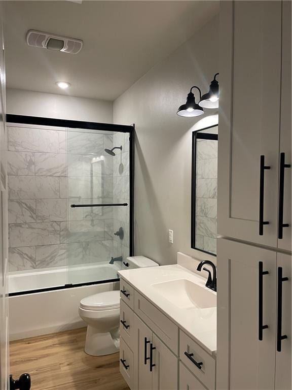 full bath featuring bath / shower combo with glass door, visible vents, toilet, vanity, and wood finished floors