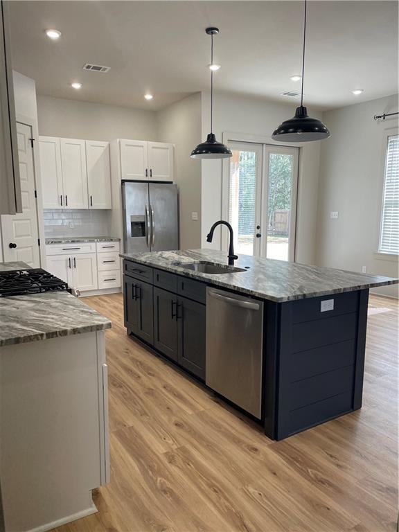 kitchen with a center island with sink, visible vents, hanging light fixtures, appliances with stainless steel finishes, and white cabinetry