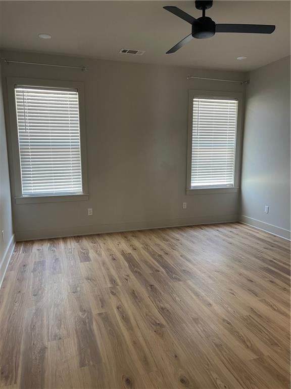 spare room with light wood-type flooring, ceiling fan, visible vents, and baseboards