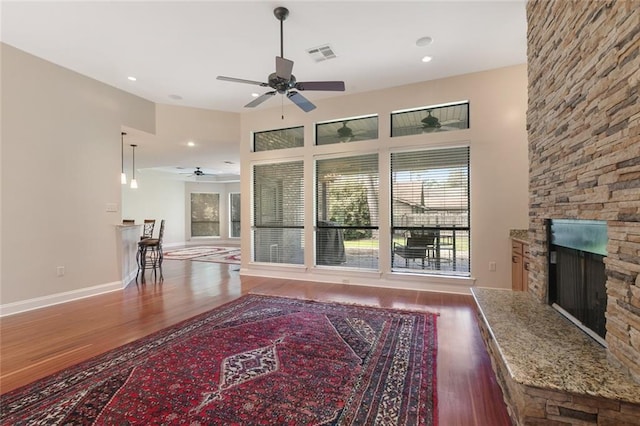 living room featuring visible vents, plenty of natural light, a stone fireplace, and wood finished floors