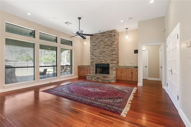 unfurnished living room with visible vents, dark wood finished floors, a stone fireplace, and a towering ceiling