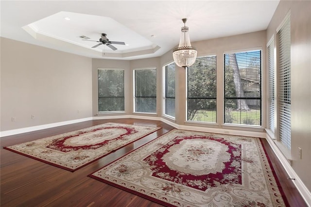 interior space featuring baseboards, visible vents, dark wood-style flooring, a tray ceiling, and ceiling fan with notable chandelier