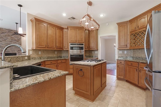 kitchen with light stone counters, a center island, hanging light fixtures, appliances with stainless steel finishes, and a sink