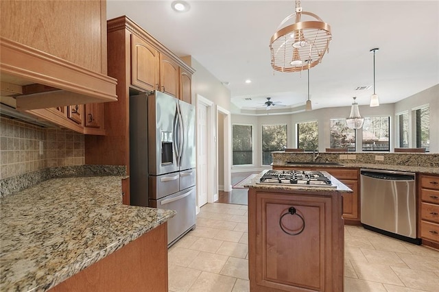 kitchen with a center island, a healthy amount of sunlight, hanging light fixtures, appliances with stainless steel finishes, and light stone countertops