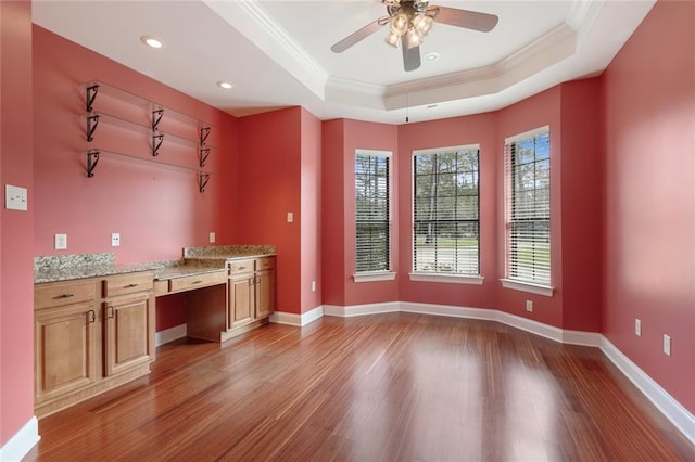 kitchen with wood finished floors, baseboards, ornamental molding, built in desk, and a raised ceiling