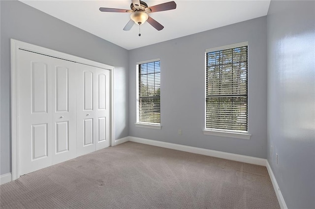 unfurnished bedroom with baseboards, ceiling fan, a closet, and light colored carpet