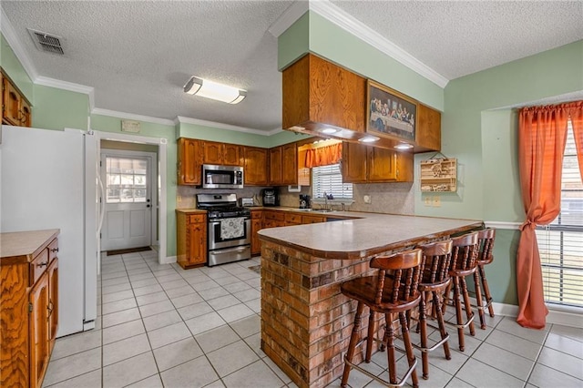 kitchen featuring appliances with stainless steel finishes, brown cabinetry, a peninsula, and light tile patterned floors