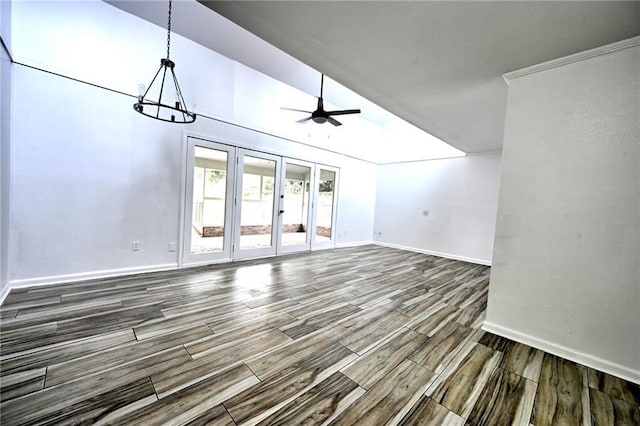 unfurnished living room with lofted ceiling, ceiling fan with notable chandelier, wood finish floors, baseboards, and french doors