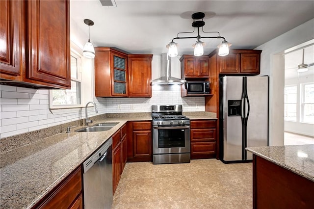 kitchen with stainless steel appliances, hanging light fixtures, backsplash, a sink, and wall chimney exhaust hood