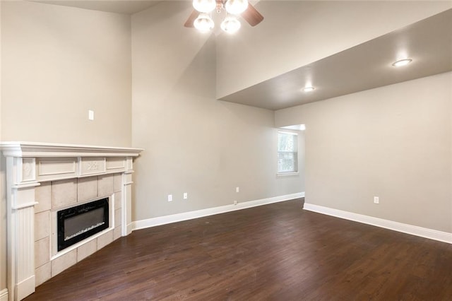 unfurnished living room with dark wood-style flooring, a tiled fireplace, a ceiling fan, and baseboards