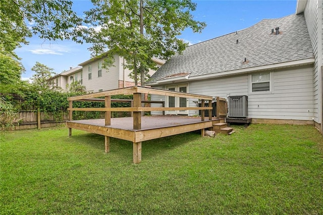 rear view of house with a shingled roof, a lawn, a deck, and fence