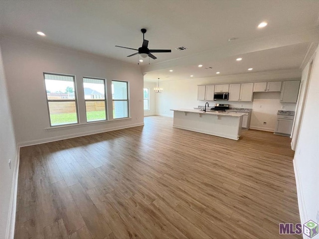 kitchen with appliances with stainless steel finishes, open floor plan, a chandelier, light wood-type flooring, and light countertops