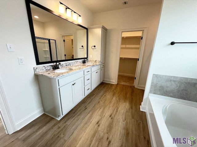 full bathroom with wood finished floors, a garden tub, a spacious closet, double vanity, and baseboards