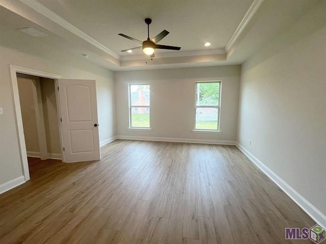 unfurnished bedroom featuring a raised ceiling, wood finished floors, ornamental molding, baseboards, and a ceiling fan