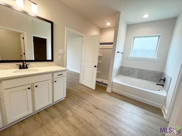 full bath featuring wood finished floors, a garden tub, vanity, recessed lighting, and a spacious closet