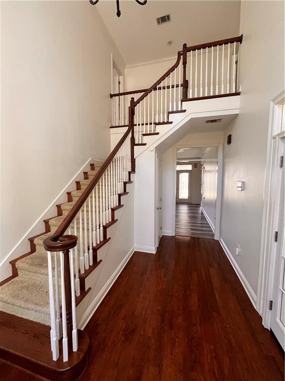 stairway with baseboards, a high ceiling, visible vents, and wood finished floors