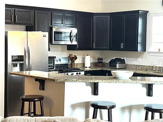 kitchen featuring stainless steel appliances, dark cabinetry, and a kitchen breakfast bar