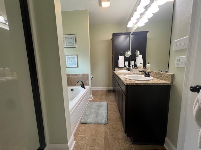 bathroom with a garden tub, double vanity, a sink, and baseboards