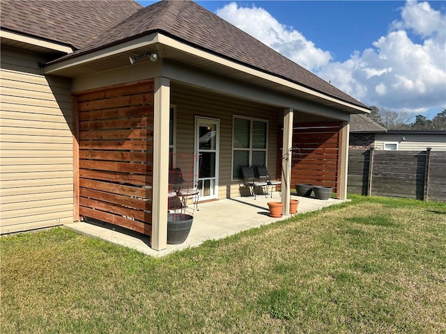 back of property featuring a shingled roof, fence, a lawn, and a patio