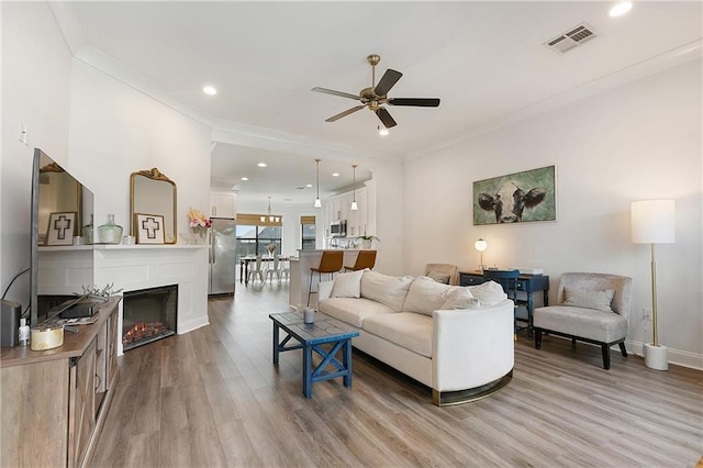 living area with recessed lighting, visible vents, crown molding, and wood finished floors