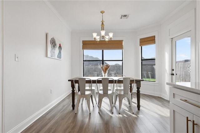 dining space with a chandelier, wood finished floors, visible vents, baseboards, and ornamental molding