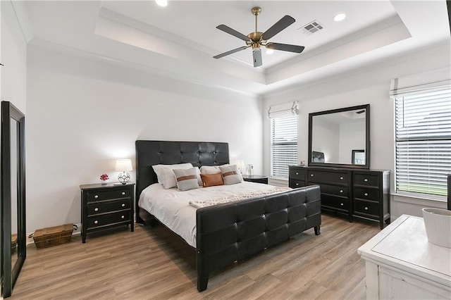 bedroom featuring light wood-style flooring, multiple windows, visible vents, and a raised ceiling