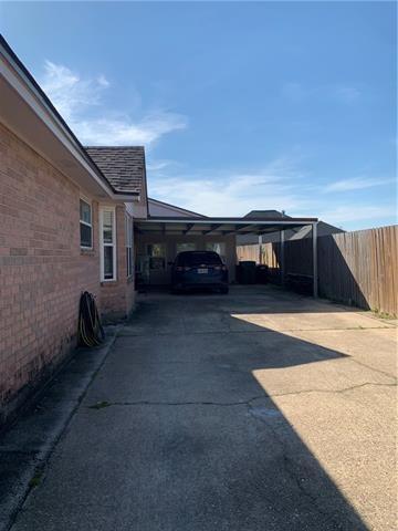 view of property exterior with an attached carport, brick siding, fence, and driveway