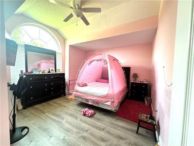 bedroom with ceiling fan, vaulted ceiling, a textured ceiling, and wood finished floors