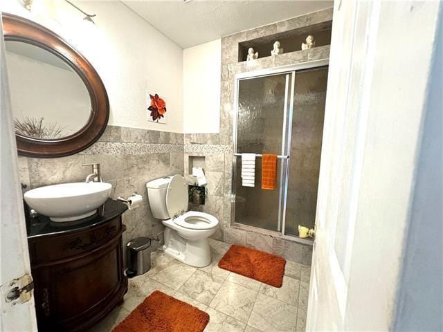 bathroom featuring a stall shower, toilet, a wainscoted wall, vanity, and tile walls