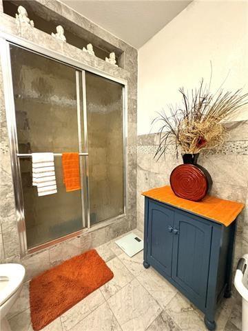 bathroom with a stall shower, tile walls, and toilet