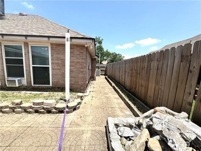 view of property exterior with a patio, brick siding, roof with shingles, and fence