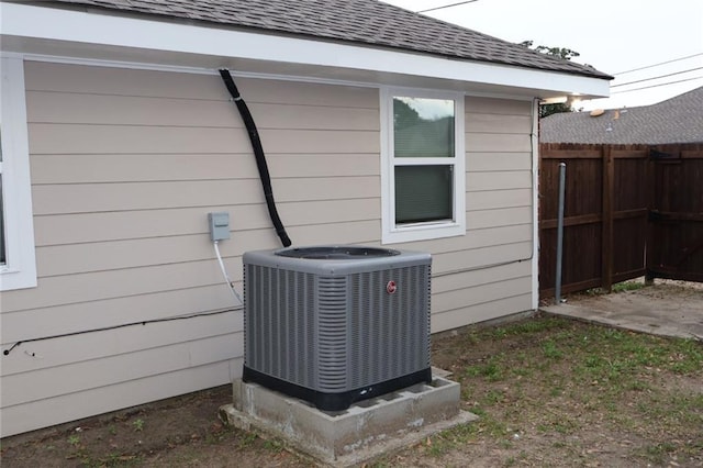 exterior details with fence, central AC, and roof with shingles