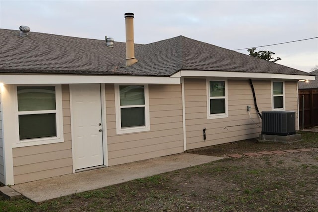 back of house with central AC and roof with shingles