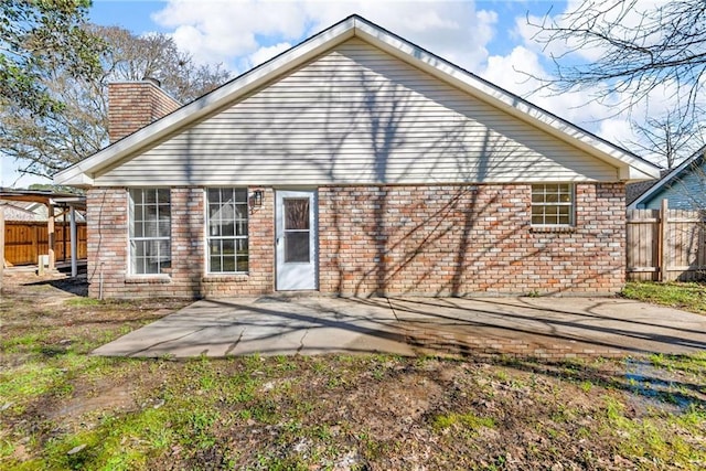 back of property with brick siding, fence, a chimney, and a patio