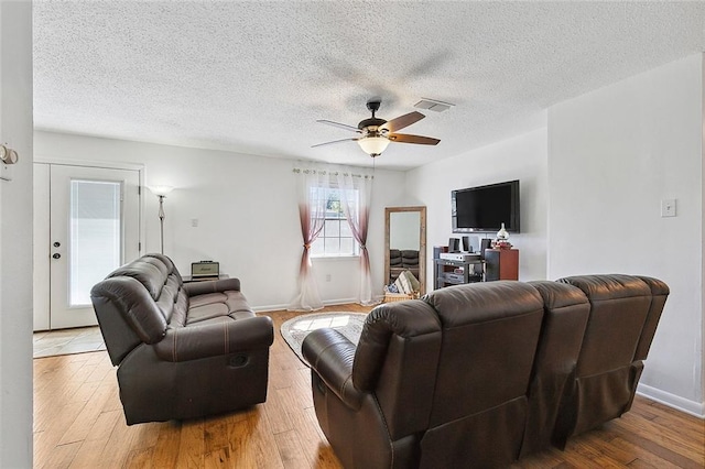 living room featuring a textured ceiling, wood finished floors, visible vents, baseboards, and a ceiling fan