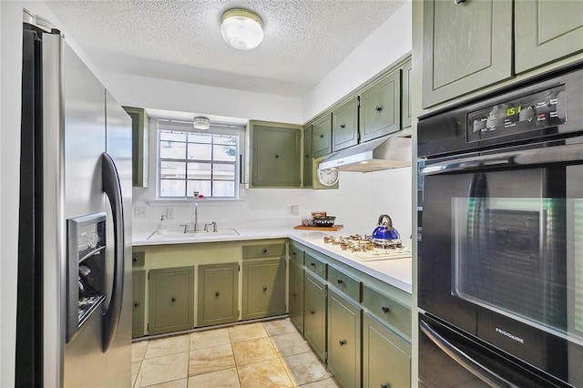 kitchen featuring oven, under cabinet range hood, a sink, green cabinets, and stainless steel refrigerator with ice dispenser